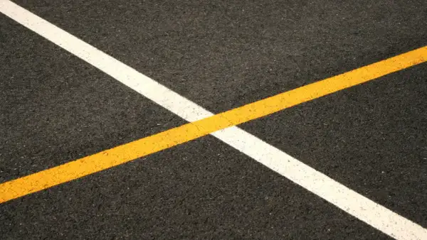 Nowe malowanie pasów drogowych: biała i żółta linia przecinają się na ciemnym asfalcie, tworząc geometryczny wzór.
