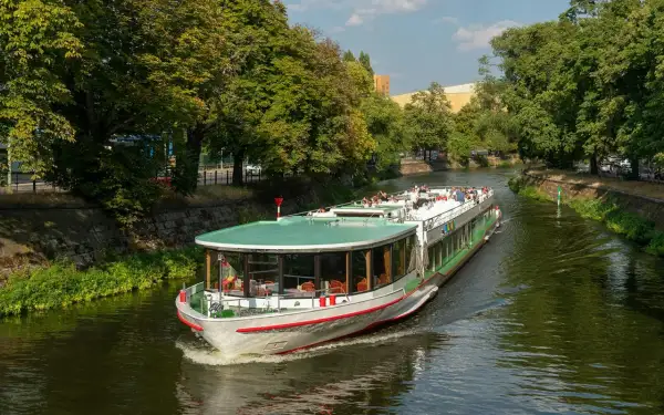 Statek wycieczkowy płynie po zielonej rzece w Berlinie, otoczony drzewami.