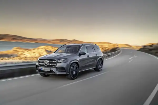Szary Mercedes GLS 580 sunie po krętej drodze nad brzegiem morza podczas zachodu słońca.