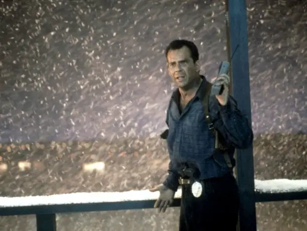 John McClane, med en gammal mobiltelefon i handen, står i snöstormen. Han är en del av rollistan i Die Hard 2.
