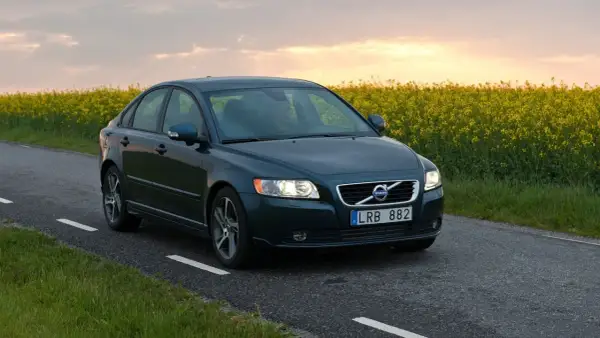 Ciemnozielone Volvo S40 2.0 diesel jedzie wiejską drogą pośród kwitnącego rzepaku o zachodzie słońca.