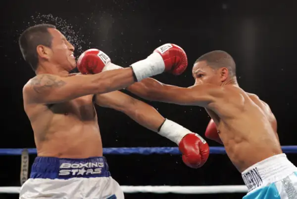Two boxers in the minimum weight category exchange blows in a tense match. One fighter recoils as a punch lands, sending sweat flying.