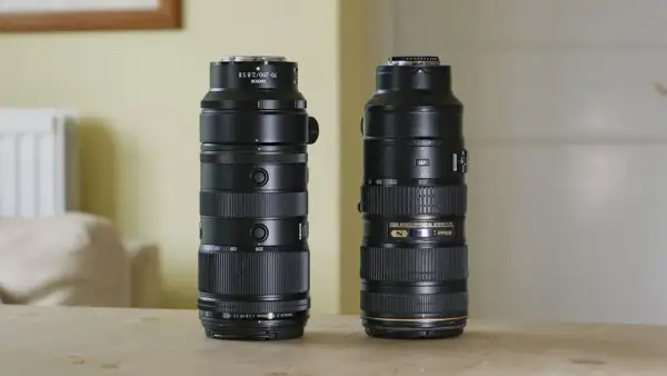 Two Nikon telephoto lenses, including a Nikkor 200mm f2, stand side-by-side on a wooden table.