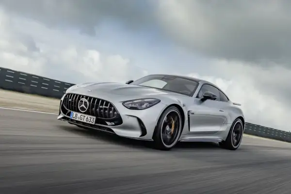 Srebrny Mercedes-AMG GT 63 sunie po torze wyścigowym, chmury na niebie podkreślają dynamikę jazdy.