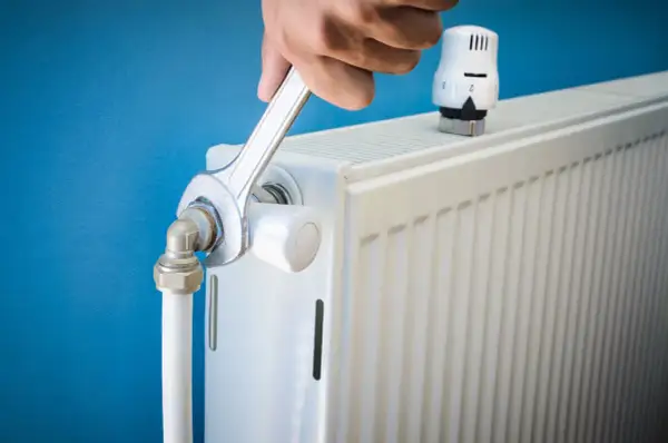 Réparation d'un radiateur bruyant. Une clé serre un raccord, peut-être pour arrêter l'eau qui coule.