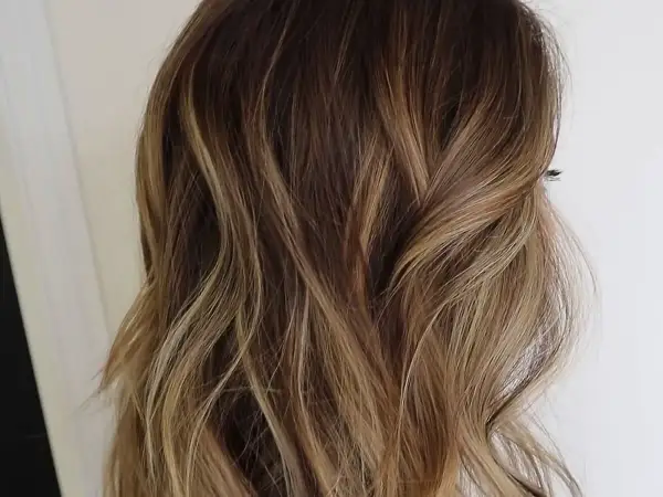 Cabello ondulado con un degradado de rubio a raíz castaña, con reflejos dorados que le dan luz.