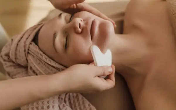 Un viso rilassato riceve un massaggio con pietra gua sha, una tecnica che serve a migliorare la circolazione e il drenaggio linfatico, donando luminosità.