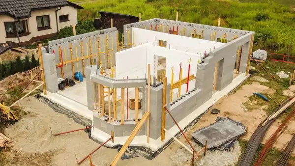 Budowa domu energooszczędnego z bloczków betonowych i białych płyt izolacyjnych. Widać zbrojenia i elementy konstrukcyjne.