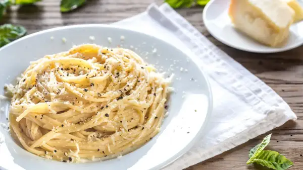 Un piatto di spaghetti fumanti conditi con abbondante cacio e pepe, guarniti con pecorino grattugiato e pepe nero macinato fresco.