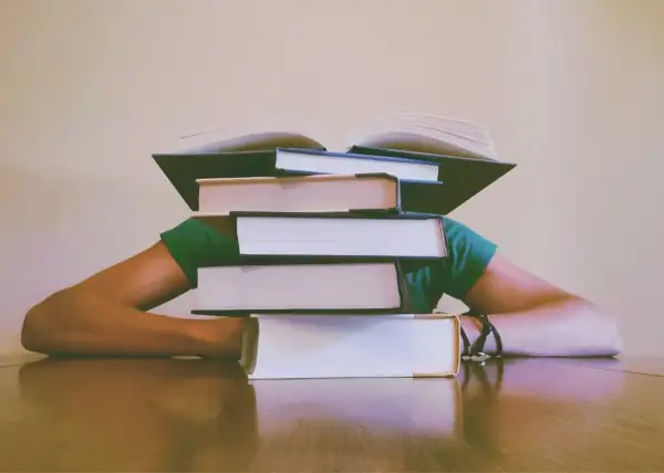 Stos książek przygniata głowę studenta. Jak napisać dyskusję w pracy magisterskiej? Czas na naukę!