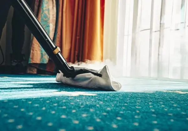 Dampfreiniger reinigt einen blauen Teppich mit Muster. Dampf steigt auf, während die Düse über den Boden gleitet.