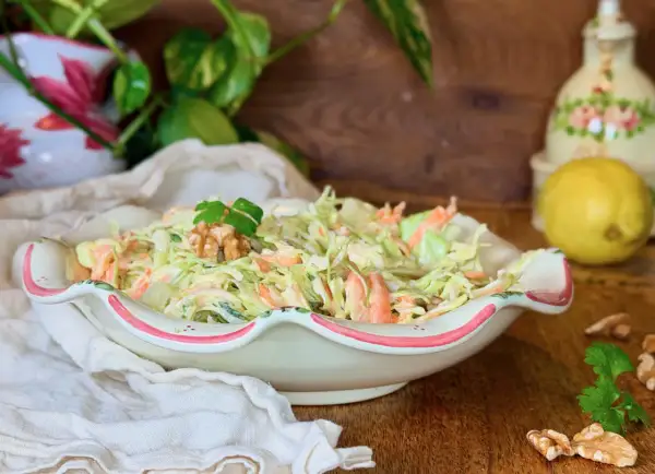 Deliciosa ensalada de col cremosa con zanahoria rallada, coronada con nueces y perejil. Perfecta para acompañar cualquier comida.