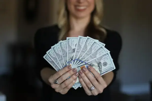 Uśmiechnięta kobieta trzyma wachlarz banknotów 100-dolarowych. Czy Vivus wyplaca w sobotę?