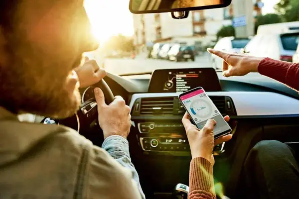 Kierowca i pasażerka sprawdzają nawigację w telefonie, ustalając trasę i czas podróży.