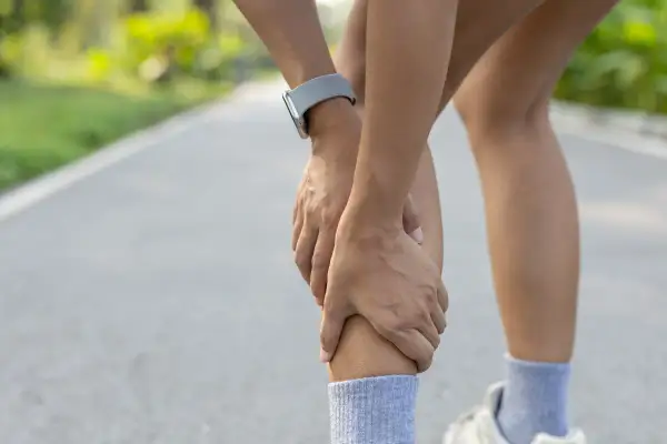 Un corridore si tiene la gamba, con le mani che stringono il polpaccio. Il tutore al polso è visibile. Il tutore mi fa male.