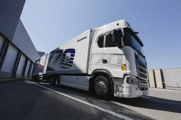 Un camion blanc Scania 770S avec une remorque, garé devant un bâtiment industriel sous un ciel bleu clair.