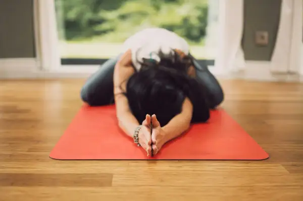 Mujer en postura de niño en esterilla roja, practicando una de las 20 posturas de yin yoga.