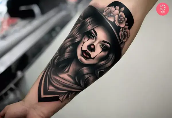 Un tatuaje chicano de una mujer con maquillaje de payaso, sombrero de copa adornado con rosas y cabello ondulado.
