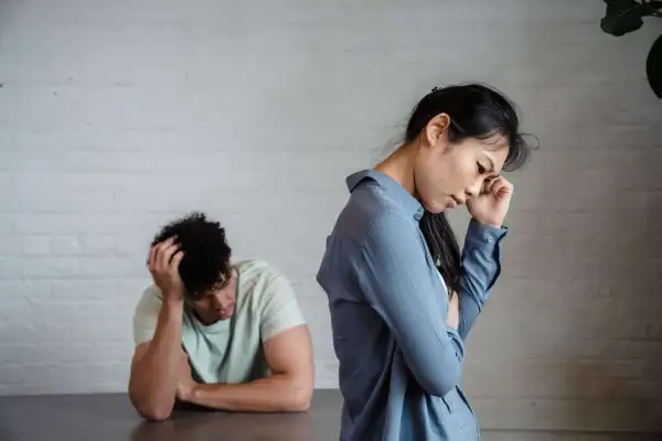 Pareja con intermitencia emocional, ella con la mano en la frente, él con la cabeza entre las manos, ambos de espaldas.