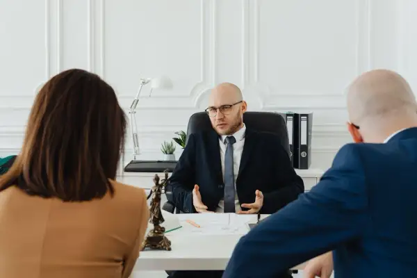 Prawnik wyjaśnia parze, jak napisać wniosek o rozwód. Na stole widać figurkę Temidy.
