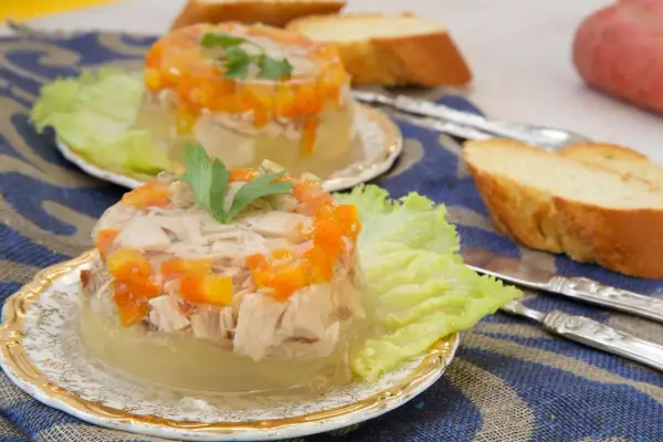 Elegancka ryba w galarecie z marchewką i natką pietruszki, podana na liściu sałaty z pieczywem.