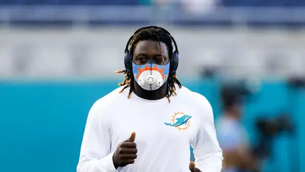 Miami Dolphins player running with an altitude mask training, headphones on, and giving a thumbs up.