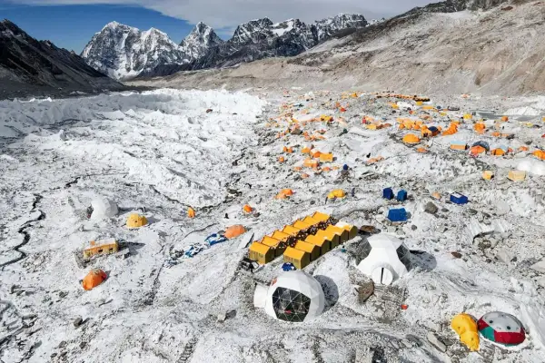 Zahlreiche bunte Zelte auf schneebedecktem Geröllfeld am Fuße des Mount Everest. Ein Basislager, das die Herausforderungen des Gipfels widerspiegelt.