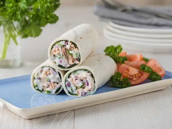 Trois wraps au thon crémeux, garnis de thon, oignons rouges et concombre, servis avec des quartiers de tomates et du persil.