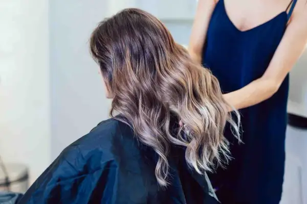 Kobieta z pięknym balejażem blond, jej włosy falują w świetle salonu.