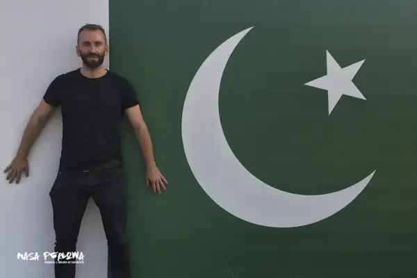 Mężczyzna w czarnym T-shircie i jeansach stoi obok flagi Pakistanu. Marzy o wizie do Pakistanu.
