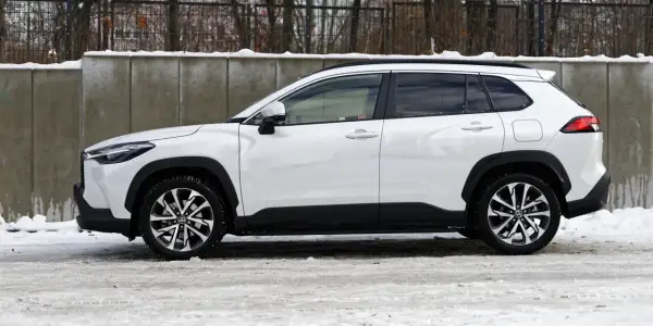 Biała Toyota Corolla Cross Hybrid na tle betonowego muru i śniegu. Stylowy SUV gotowy na zimowe wyzwania.