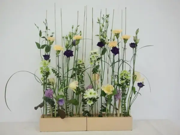 Kompozycja w stylu wegetatywnym we florystyce: delikatne kwiaty, trawy i liście tworzą naturalny, lekki ogród w prostokątnej donicy.
