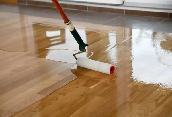 Application d'une première couche de vitrificateur sur un parquet en bois. Le rouleau laisse une surface brillante et humide.