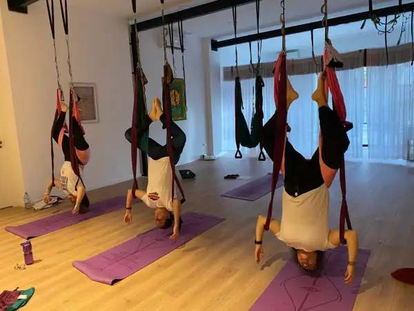 Personas practicando ahimsa yoga en columpios aéreos, invertidas y relajadas.