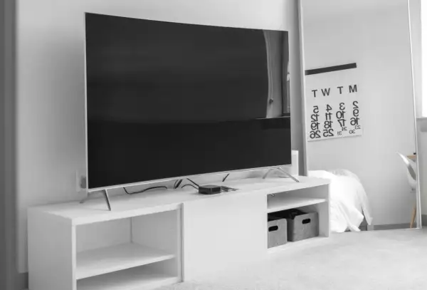 Nowoczesny salon z dużym telewizorem, którego wymiary to 75 cali, na białej szafce RTV. Obok lustro z kalendarzem.