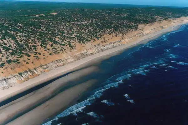 Vista aérea de la **playa de Castilla**, con dunas cubiertas de vegetación, arena dorada y el mar azul con olas.