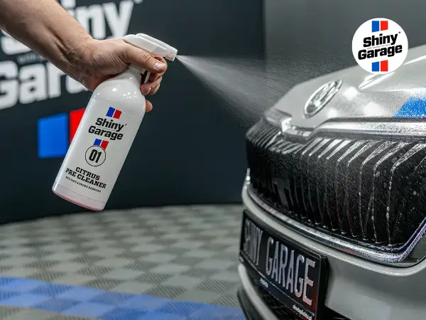 Ręka rozpyla pre-wash oprysk Citrus Pre Cleaner z butelki Shiny Garage na grill samochodu, usuwając brud.