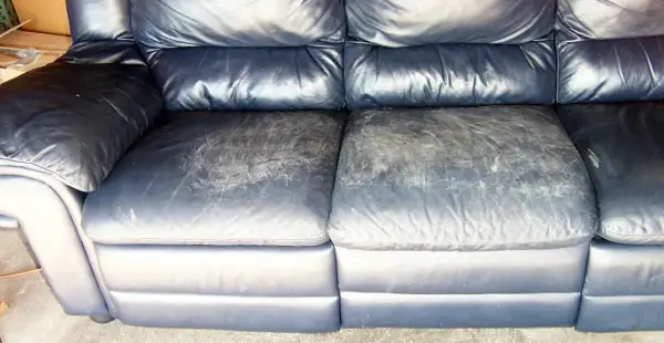A dark blue leather couch with worn, scuffed seat cushions, showing the need for restoration.