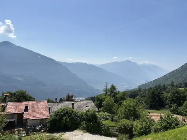 Case con tetti rossi ai piedi del monte Biaina, con valli e montagne azzurre all'orizzonte sotto un cielo limpido.