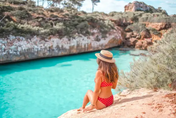 Une femme en bikini rouge à pois et chapeau de paille admire la crique turquoise. Idéal pour savoir que faire à Majorque.