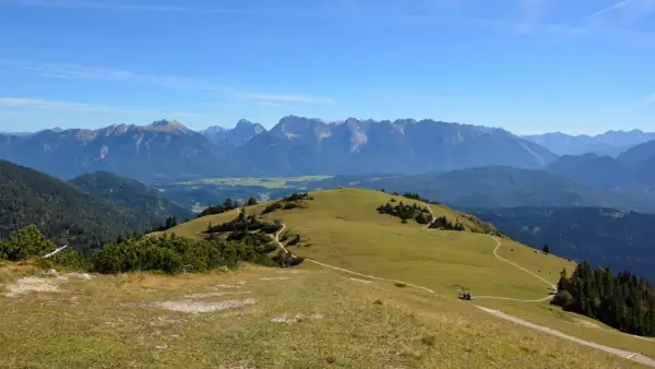 Ein sonniger Tag lädt zum **Wank wandern** ein. Grüne Hügel mit verschlungenen Pfaden erstrecken sich vor einer majestätischen Bergkulisse.
