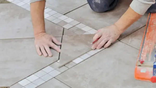 Un carreleur prépare le plan de pose du carrelage, marquant une pièce avec un crayon.