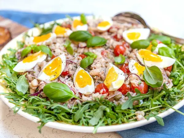 En härlig tonfisk sallad med kokta ägg, tomater, bönor och färsk basilika, serverad på en bädd av rucola.