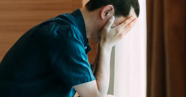 Mężczyzna z rękami na twarzy, zmartwiony. Warto znać objawy raka jądra.