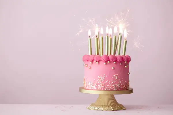 Różowy tort z gwiazdkami i złotymi świeczkami, ozdobiony różową posypką, z iskrami fajerwerków. Idealny na piękne życzenia urodzinowe.