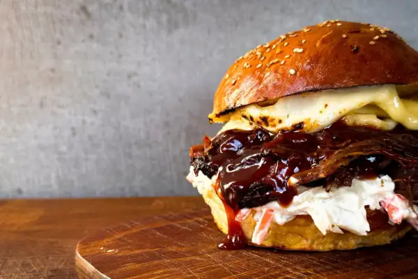 Saftiger pulled beef burger mit geschmolzenem Käse und BBQ-Sauce, serviert auf einem Holzbrett.