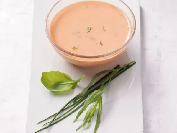 Schüssel mit cremigem French Dressing, garniert mit frischem Basilikum und Schnittlauch.