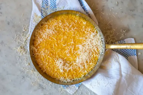 En gyllene risotto milanese, toppad med riven parmesan, i en metallpanna på en marmorskiva.