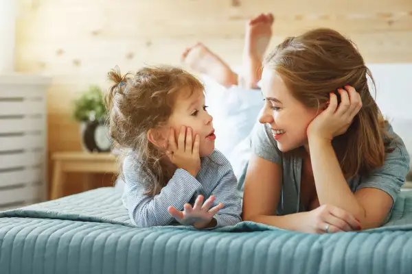 Mutter und Kind liegen auf dem Bett und sprechen. Das Kind übt emotionsregulation kinder, während die Mutter liebevoll zuhört.