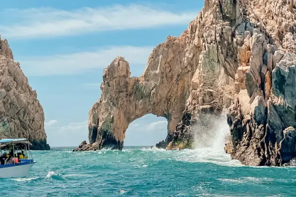 Un paseo en barco revela el Arco de Cabo San Lucas, una maravilla natural que ver en Baja California. Las olas rompen contra las rocas doradas bajo un cielo azul.